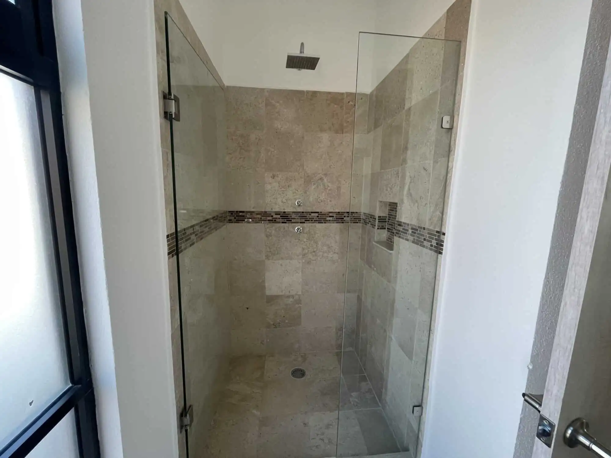 Spacious bathroom shower with glass door and beige tile walls in La Serena Residencial.