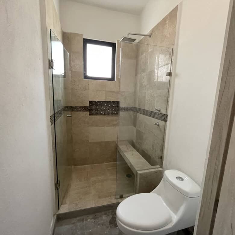 Modern bathroom with walk-in shower, bench, and small window in Santo Domingo home.
