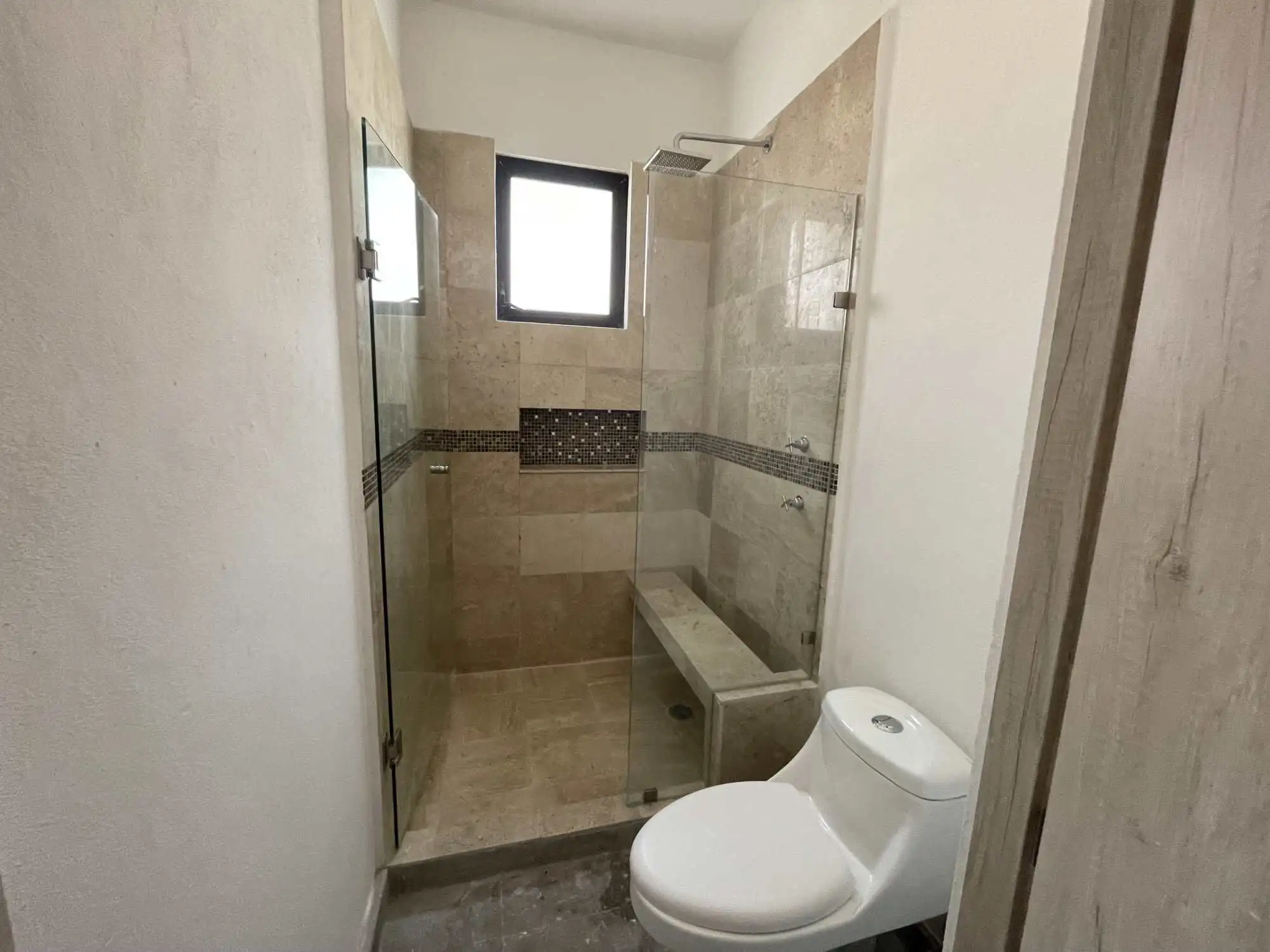 Modern bathroom with walk-in shower, bench, and small window in Santo Domingo home.