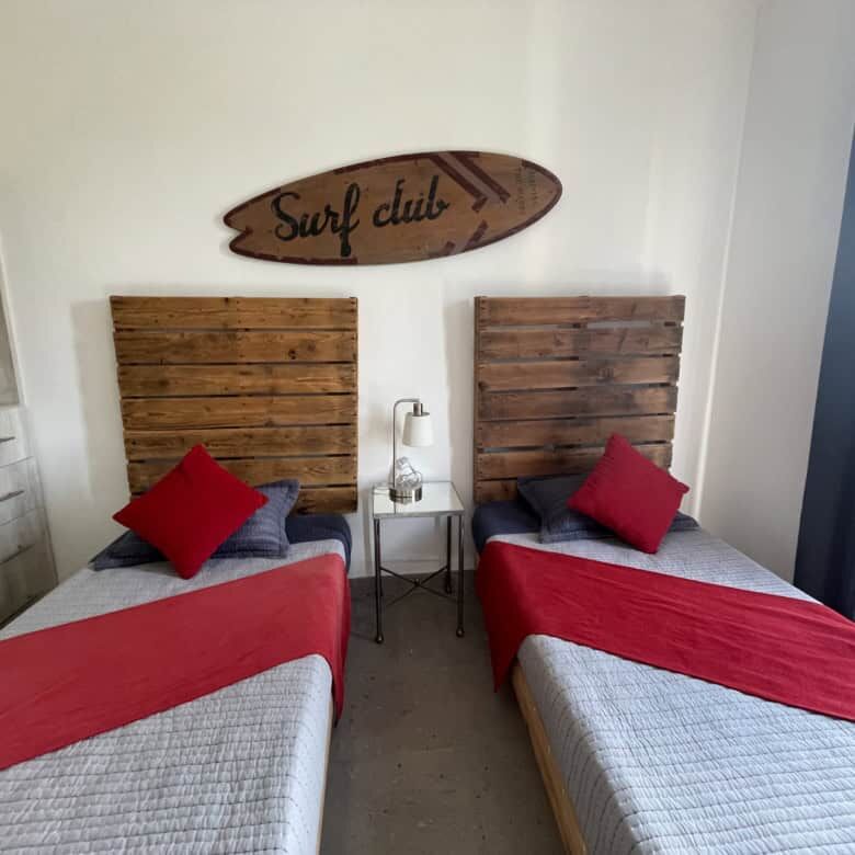 Bright bedroom featuring two single beds with red accents and wooden headboards, decorated with a su.