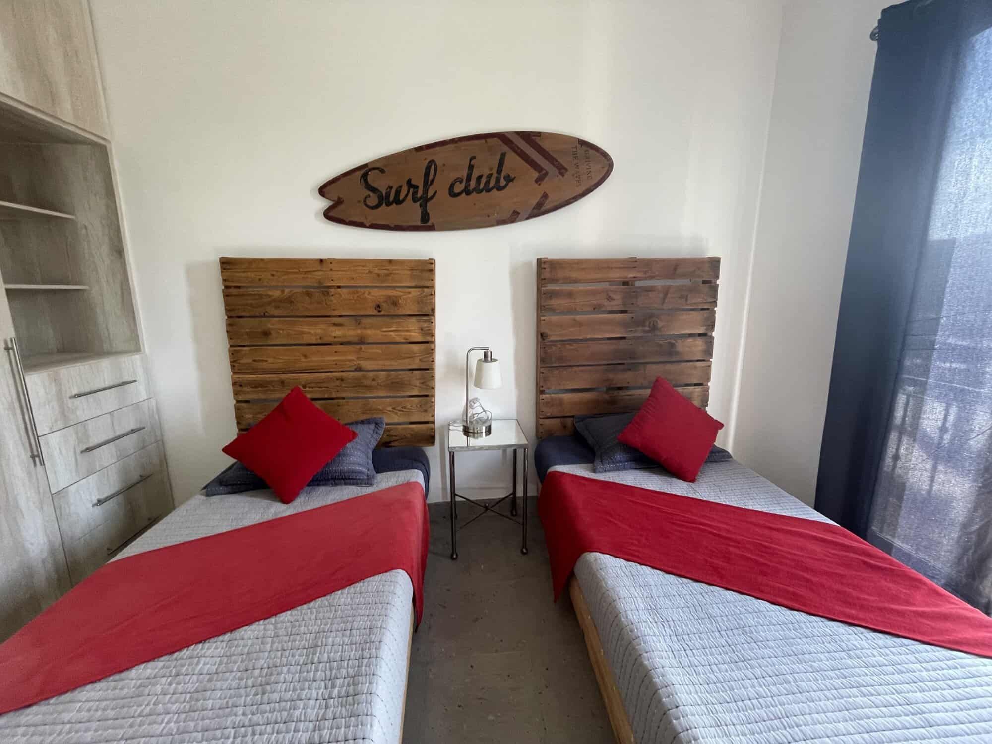 Cozy Modern Bedroom with Wooden Headboards and Surfboard Decor Bright bedroom featuring two single beds with red accents and wooden headboards, decorated with a su.