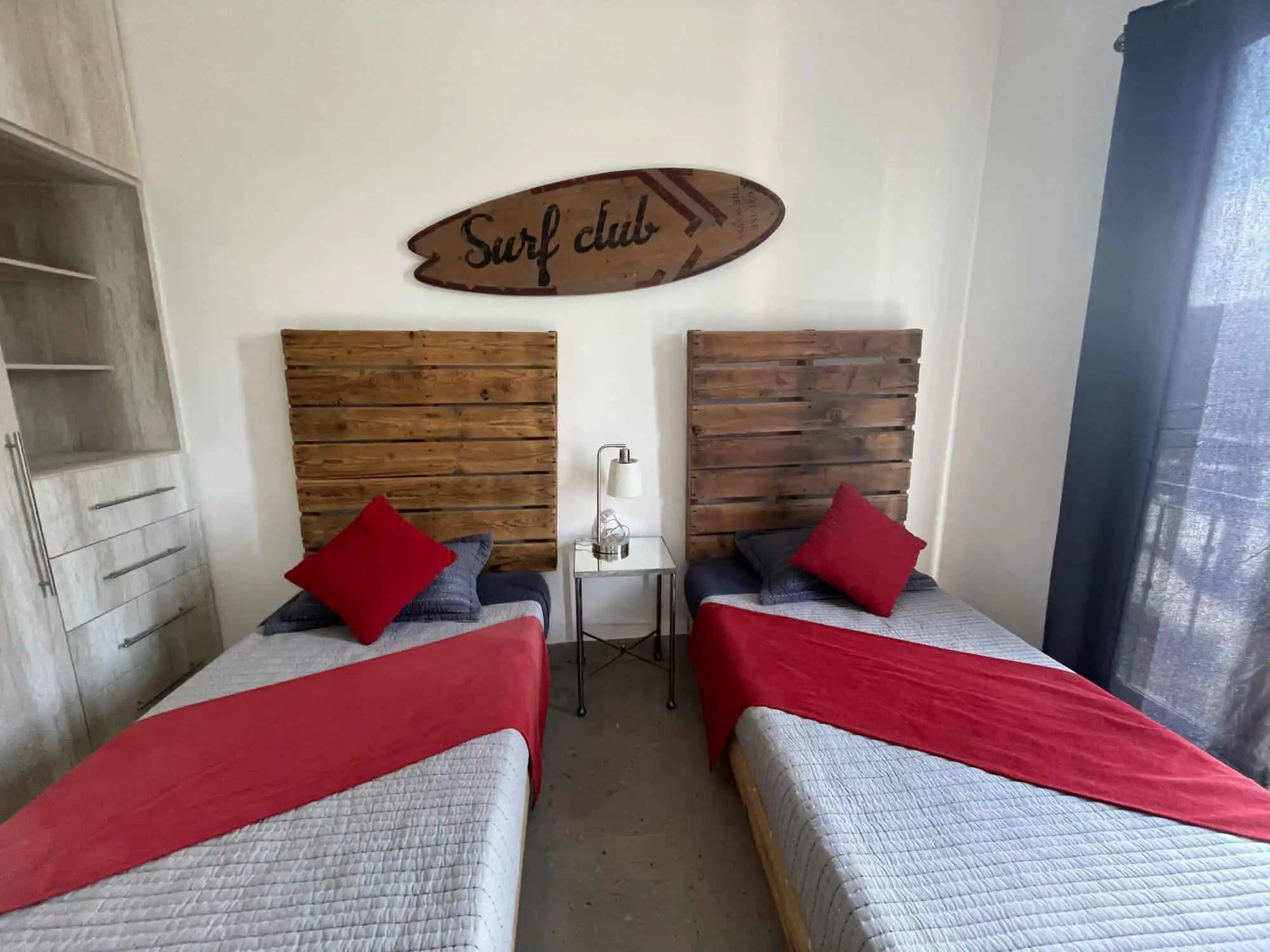 Bright bedroom featuring two single beds with red accents and wooden headboards, decorated with a su.