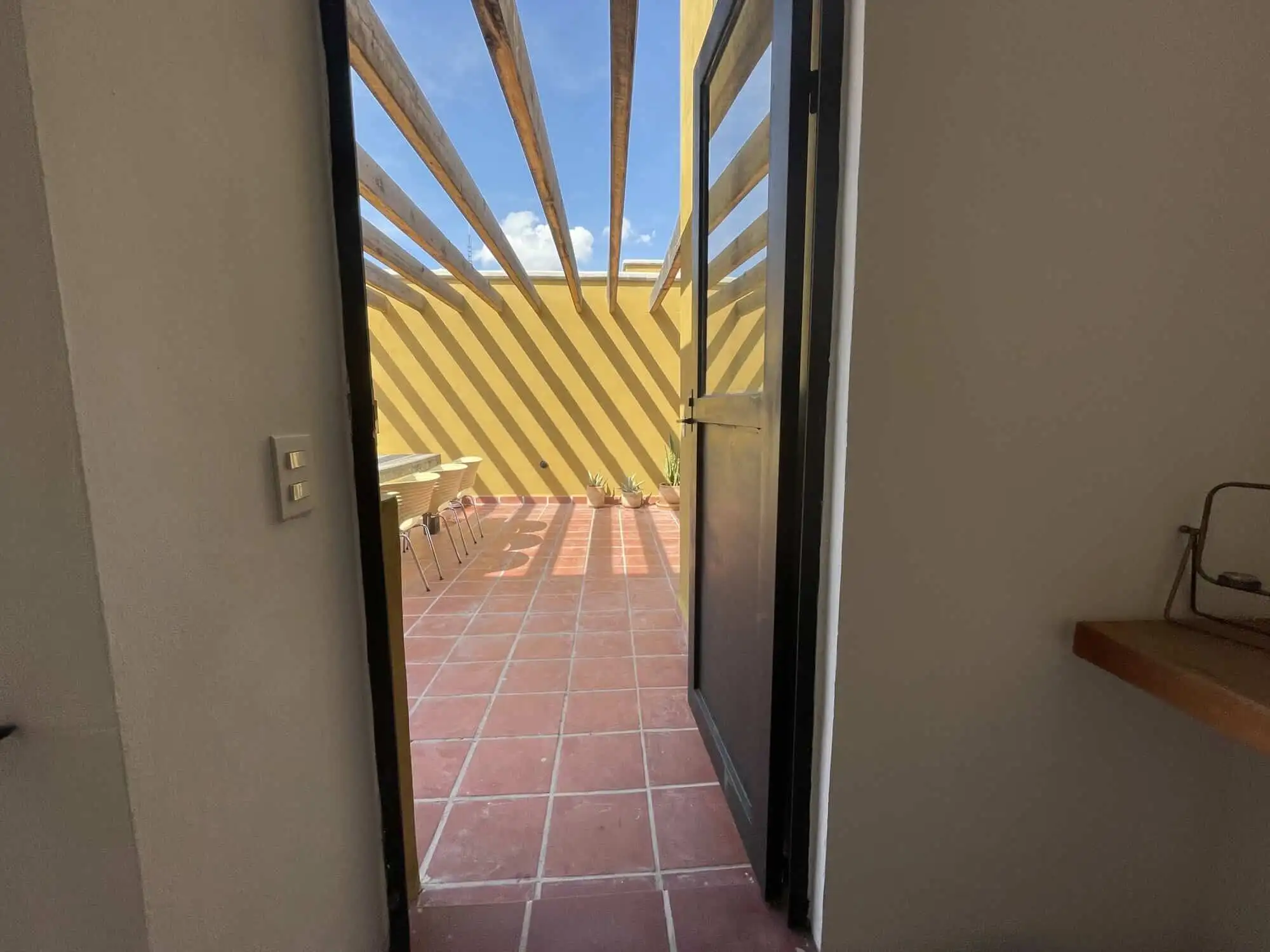 Balcony door opening to a sunny outdoor terrace with yellow and black striped railing.