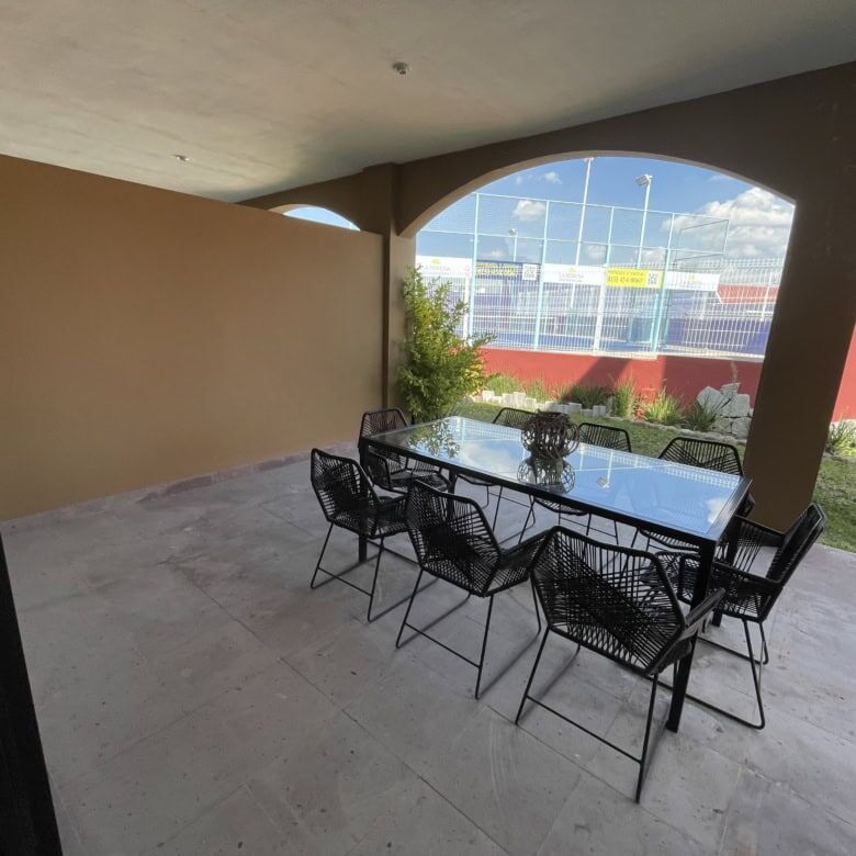 Outdoor dining area with glass table and black chairs under a covered patio.