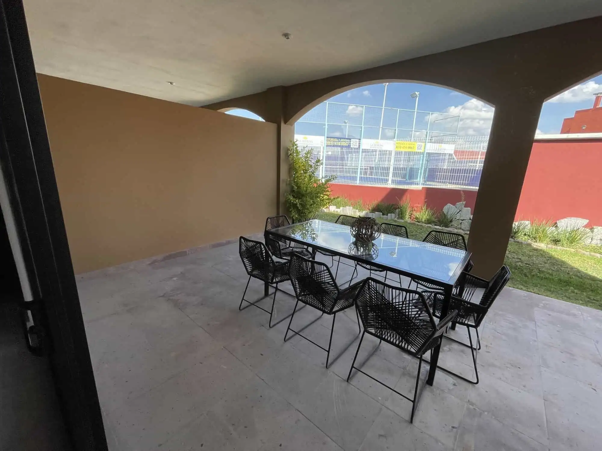 Outdoor dining area with glass table and black chairs under a covered patio.