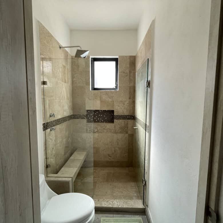 Bathroom with walk-in shower, bench, and small window in a modern colonial-style home.