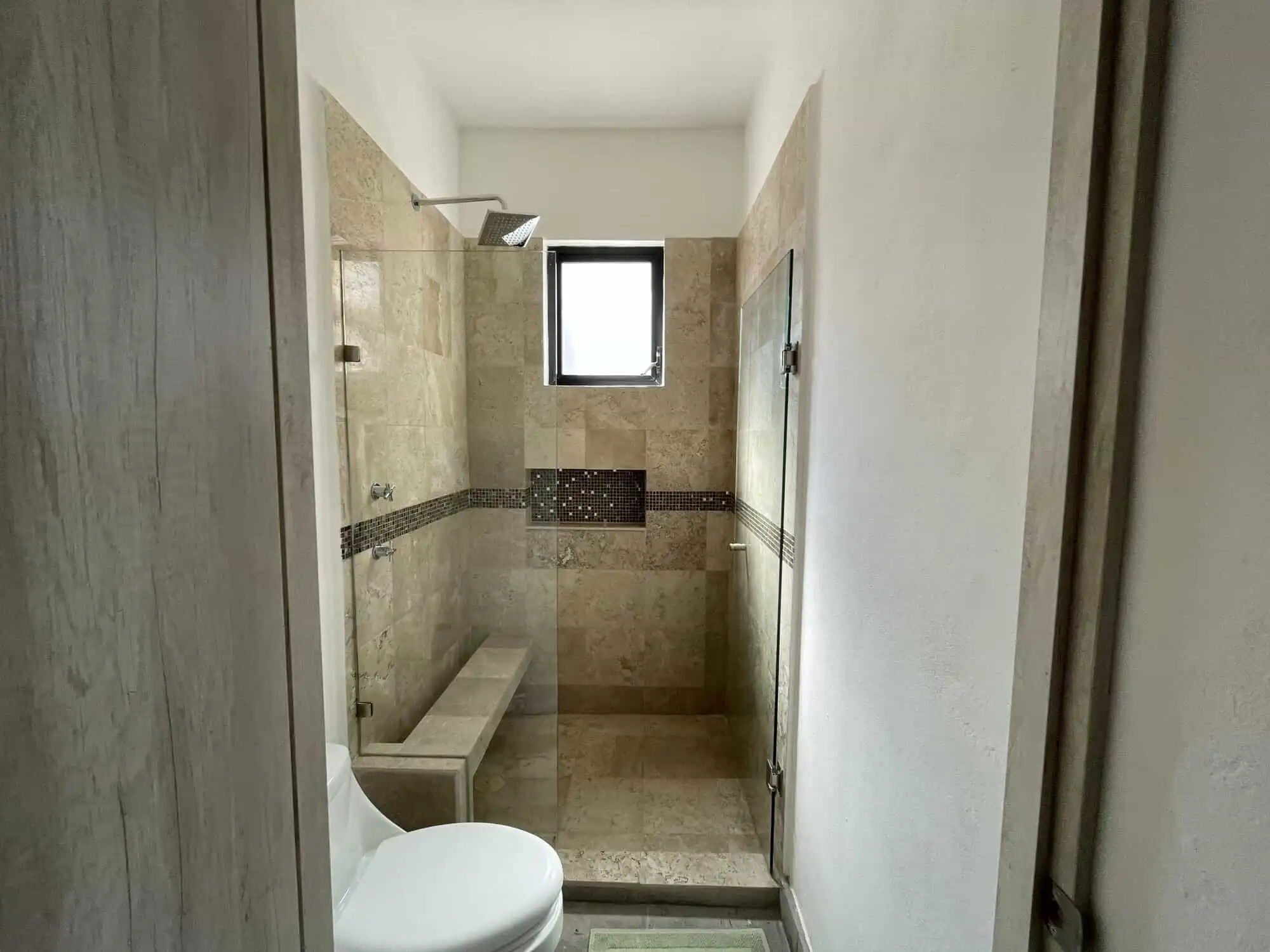 Bathroom with walk-in shower, bench, and small window in a modern colonial-style home.