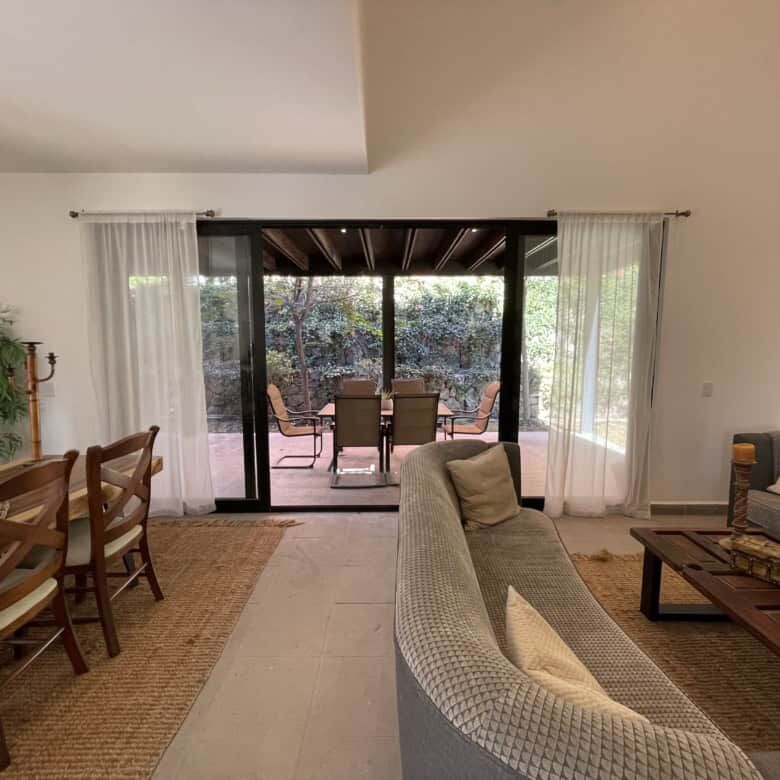 Spacious living room with sliding glass doors opening to a terrace with outdoor seating and lush gar.