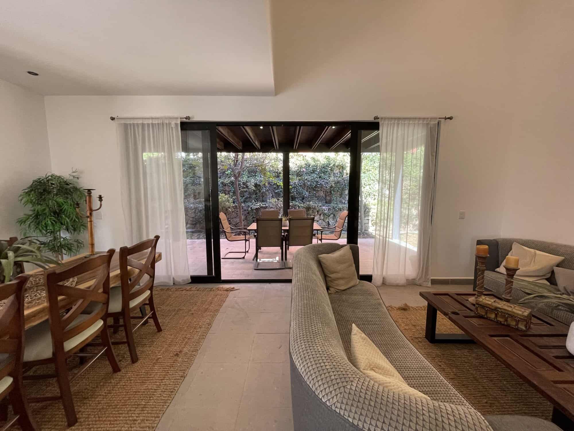 Spacious living room with sliding glass doors opening to a terrace with outdoor seating and lush gar.