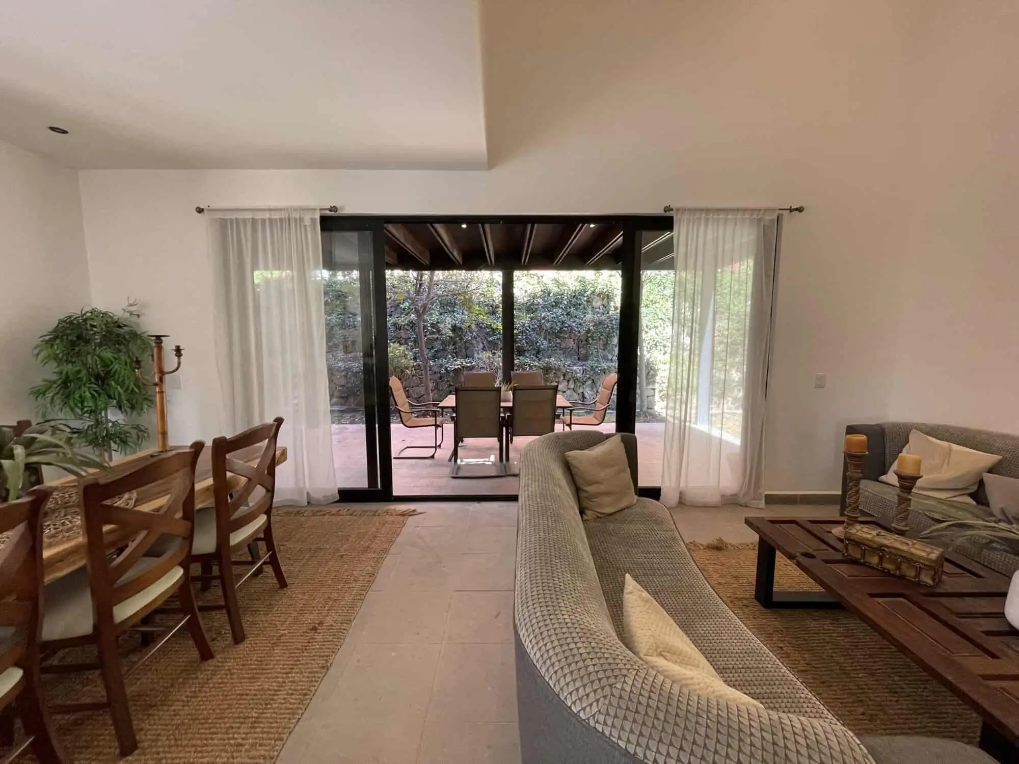 Spacious living room with sliding glass doors opening to a terrace with outdoor seating and lush gar.