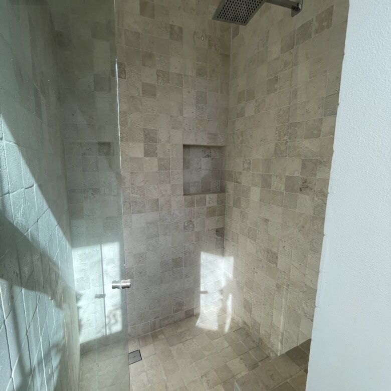 In shower with beige tiled walls and ceiling-mounted rainfall showerhead.