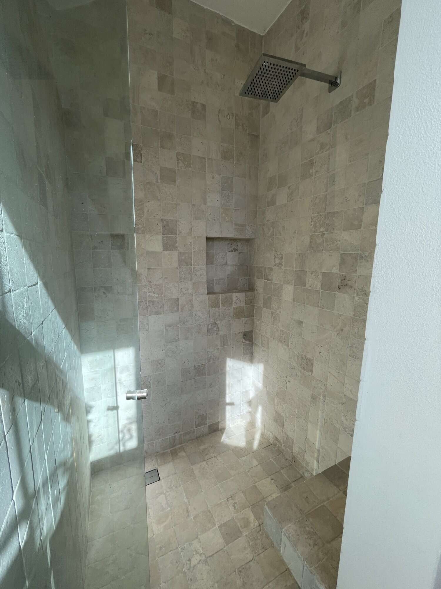 In shower with beige tiled walls and ceiling-mounted rainfall showerhead.