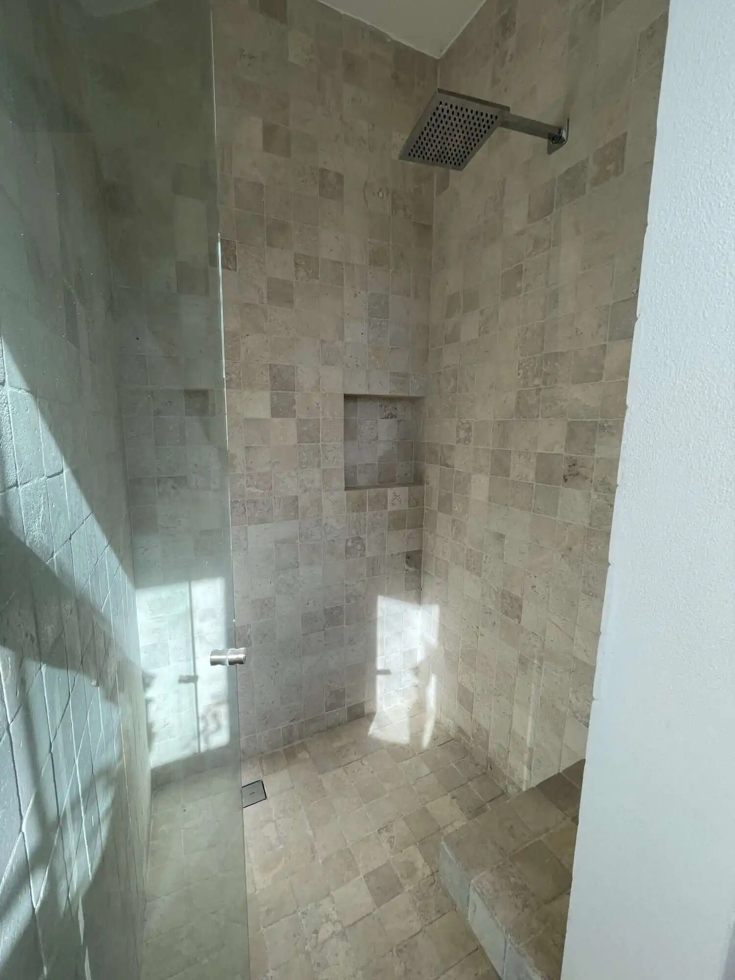 In shower with beige tiled walls and ceiling-mounted rainfall showerhead.