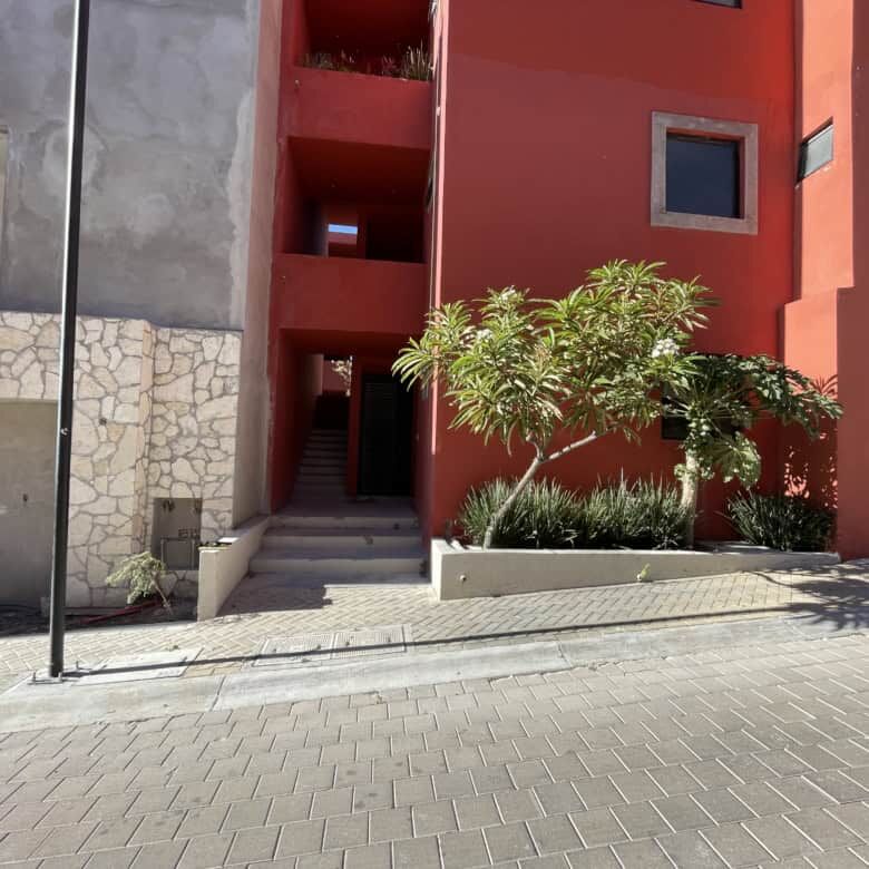 Floor home with vibrant red exterior in San Miguel de Allende, featuring lush greenery and contempor.