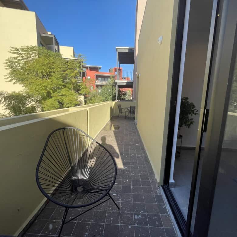 Balcony with black outdoor chair overlooking neighboring buildings and greenery.