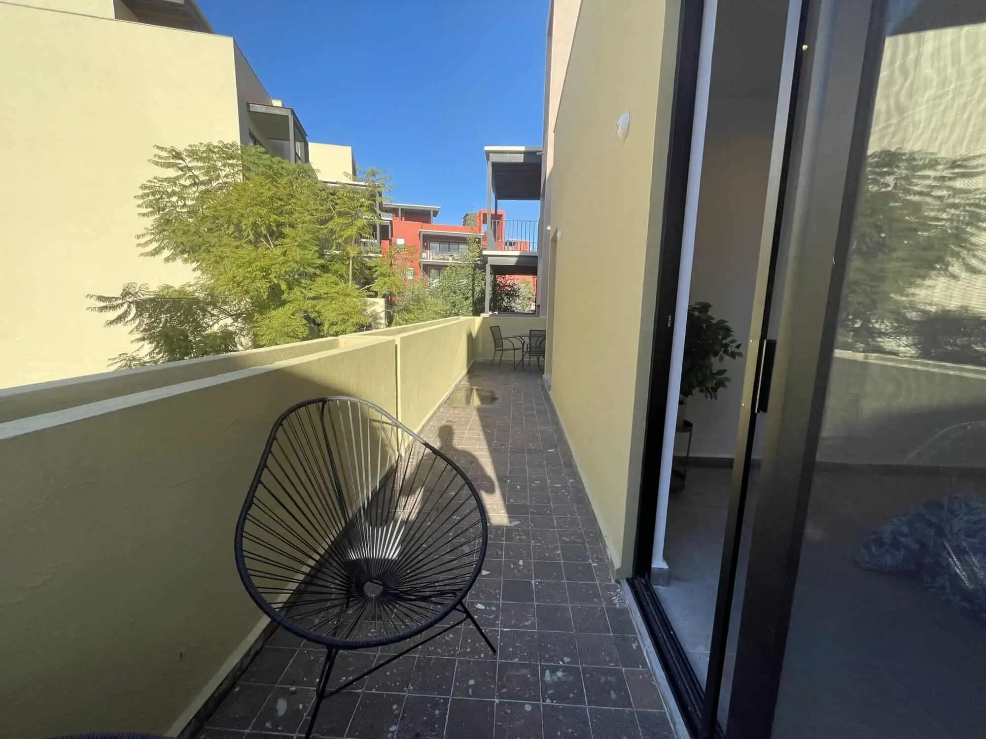 Modern balcony with outdoor seating in Punta del Cielo, San Miguel de Allende. Balcony with black outdoor chair overlooking neighboring buildings and greenery.