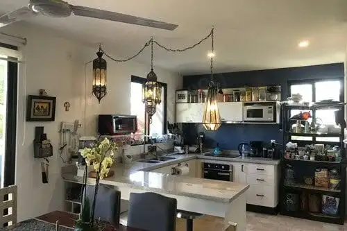 Bright, open-concept kitchen featuring white cabinetry, black backsplash, and stylish lighting fixtu.