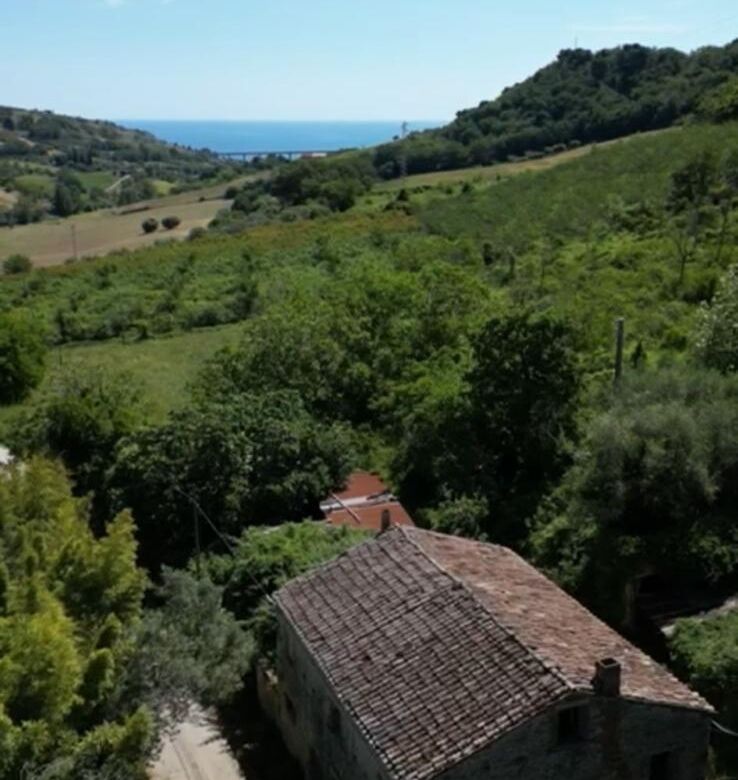 Rustic farmhouse surrounded by lush greenery with distant sea view in Campofilone, Fermo.