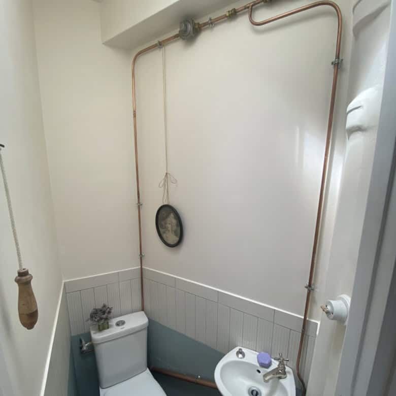 Cozy bathroom featuring exposed copper pipes and a small sink in a stylish Paris apartment.