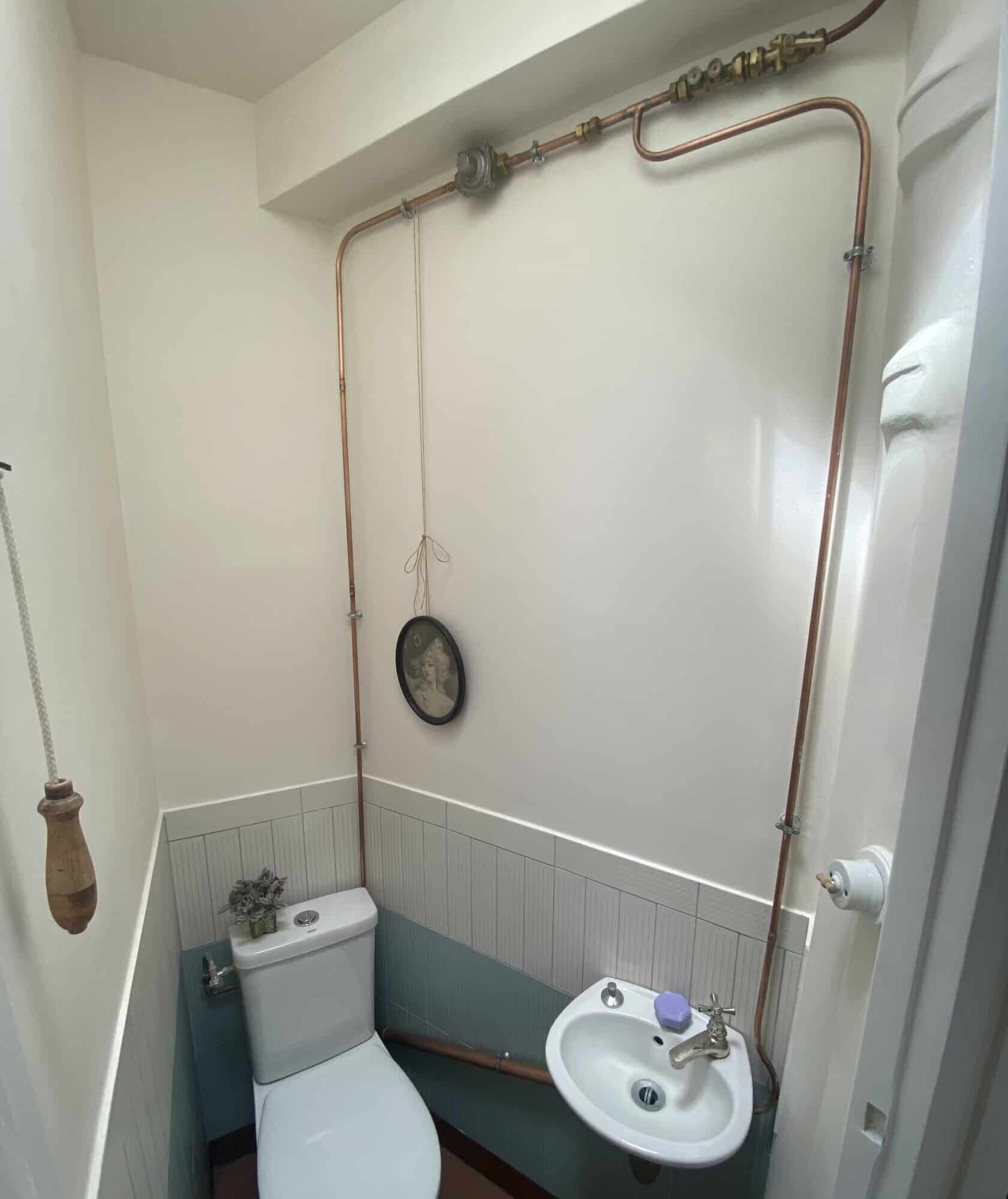 Cozy bathroom featuring exposed copper pipes and a small sink in a stylish Paris apartment.