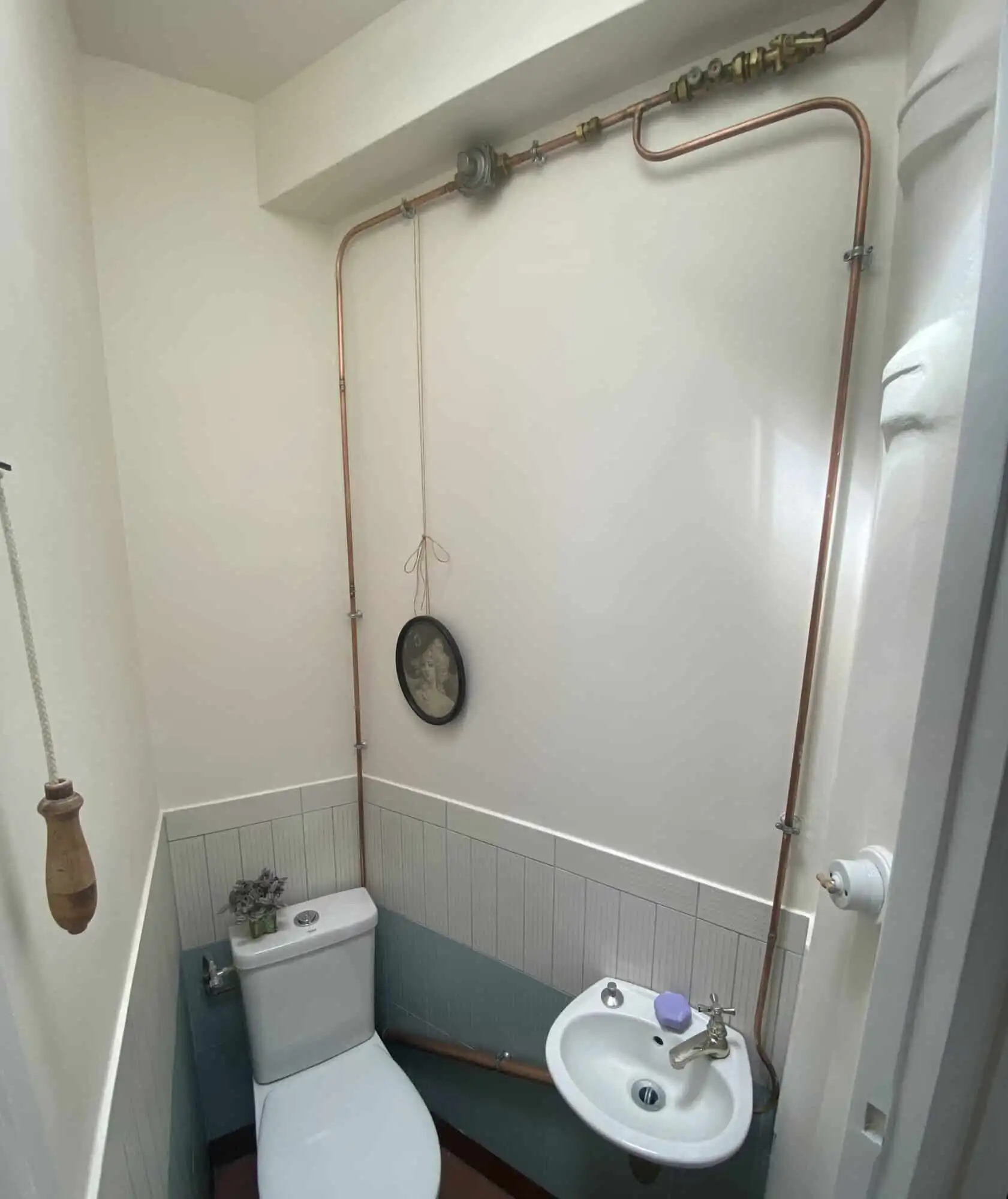 Cozy bathroom featuring exposed copper pipes and a small sink in a stylish Paris apartment.
