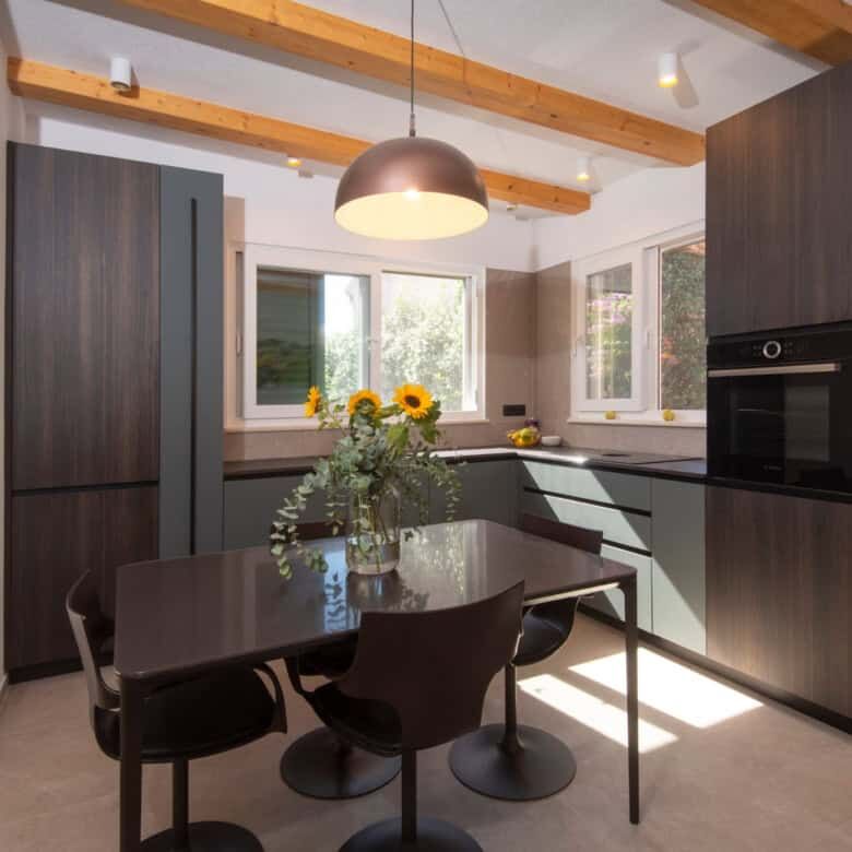 Modern kitchen with wooden ceiling beams, black cabinetry, and a dining area with a vase of sunflowe.