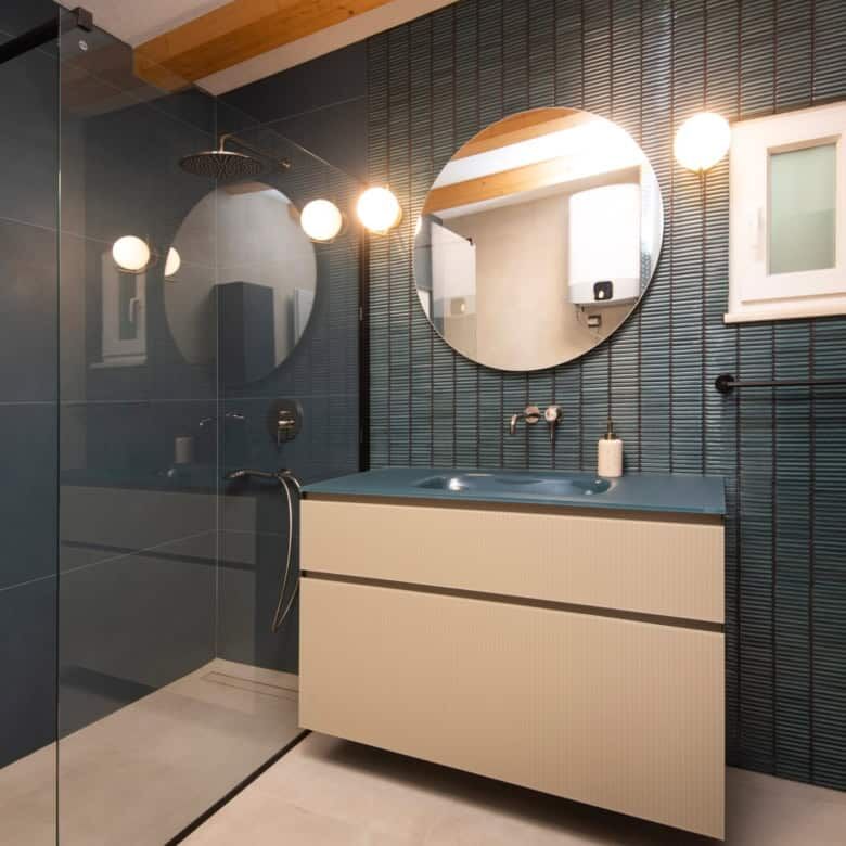 Modern bathroom featuring blue tiled walls, two round mirrors, and contemporary lighting fixtures.