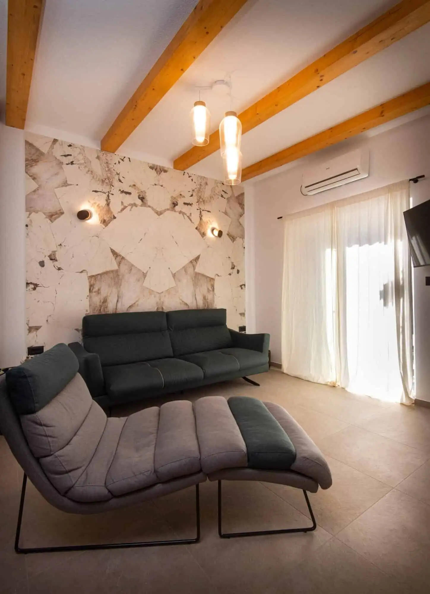 Modern living room with stylish furniture and wooden ceiling beams in Split. Contemporary living room with black sofa, lounge chair, and natural light in Split.