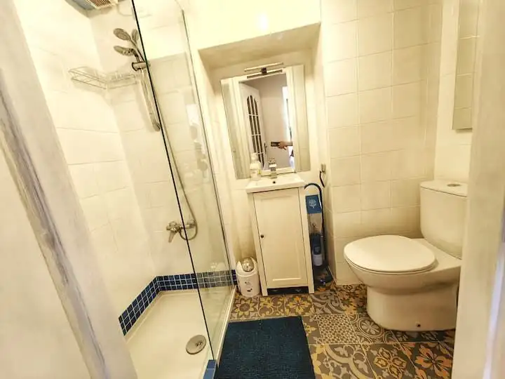 Interior view of a small apartment bathroom with shower, toilet, and storage cabinet.