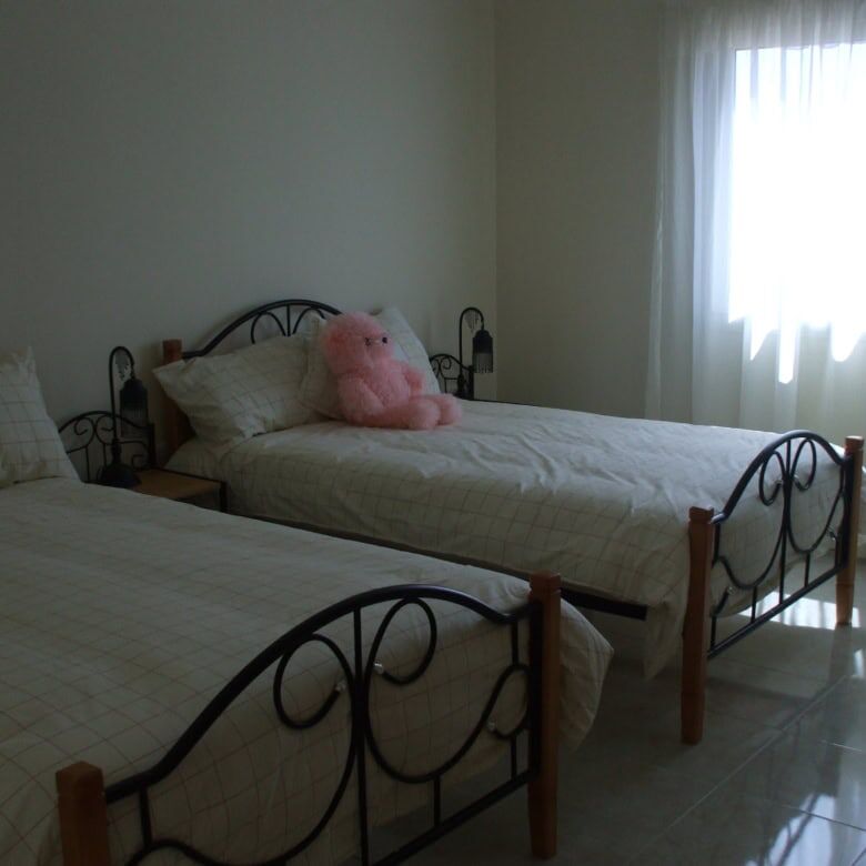 Comfortable bedroom with twin beds and a pink teddy bear, bright natural light from window.