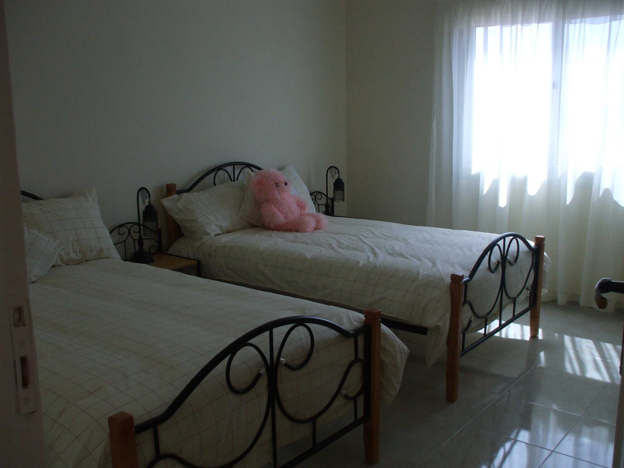 Luxury 1 Bed Apartment in Oasis 5 Hurghada Comfortable bedroom with twin beds and a pink teddy bear, bright natural light from window.