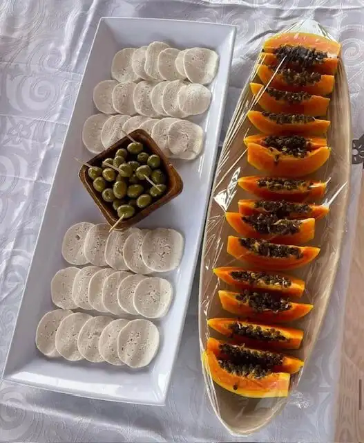 Delicious sliced papaya with black seeds and a platter of bread and olives.