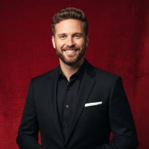 Businessman in formal suit smiling on red backdrop.