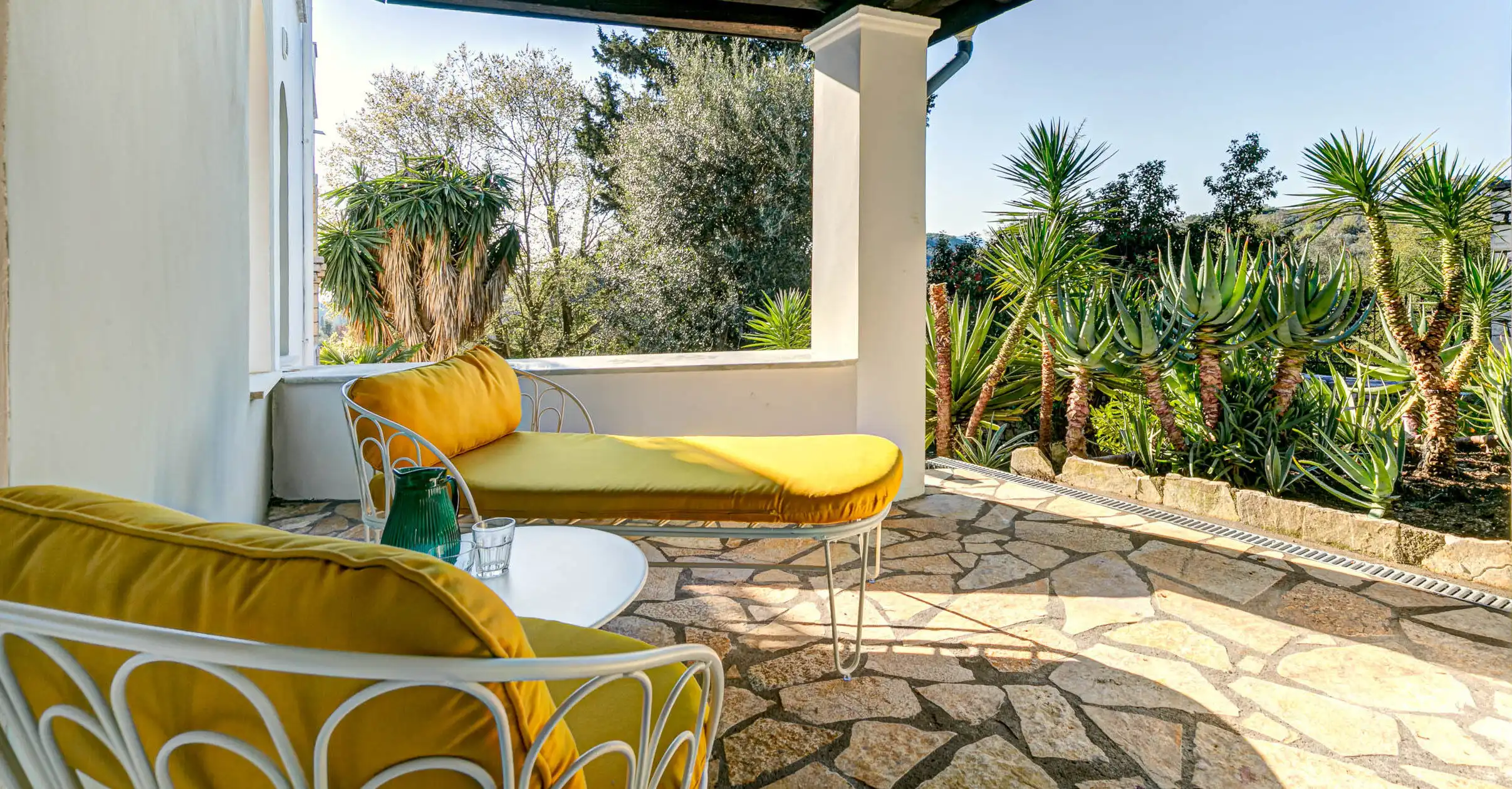 View Villa Gouvia Corfu View terrace with lounge chairs in a lush garden setting.