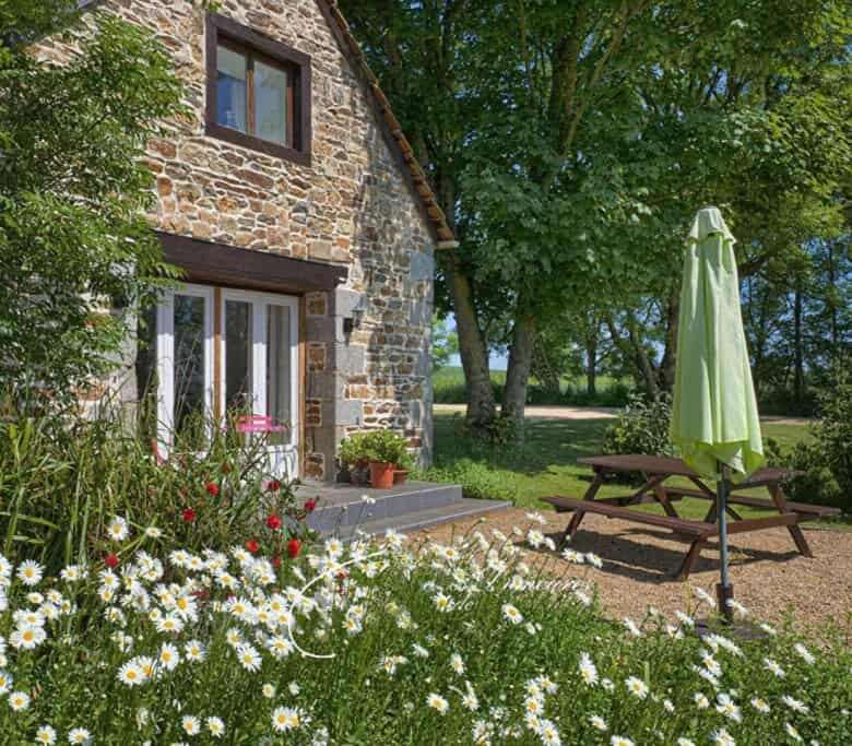 Charming stone cottage with garden, outdoor seating, and lush greenery in Brittany.
