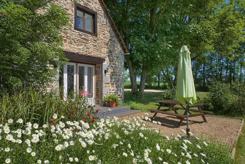 Charming stone cottage with garden, outdoor seating, and lush greenery in Brittany.