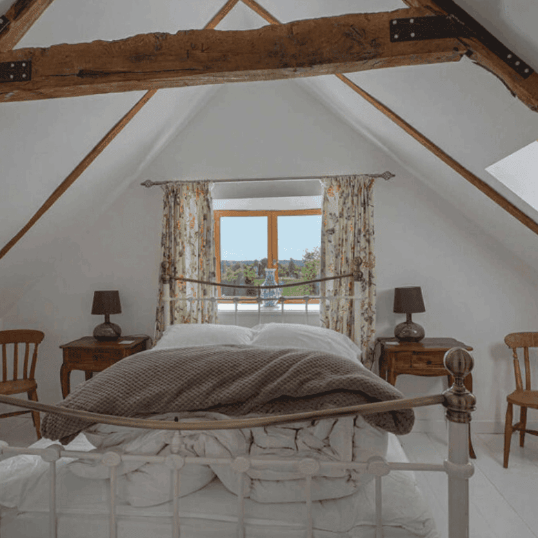 Cozy bedroom in Brittany featuring exposed wooden beams, a large window, and traditional decor. Perf.