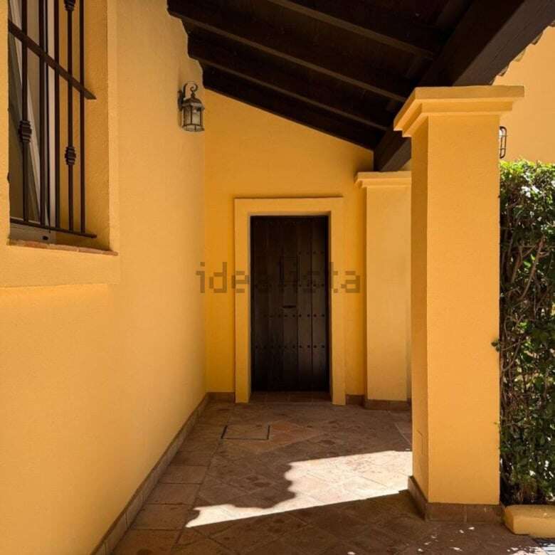 Elegant villa entrance with shaded porch, yellow walls, and surrounding garden in Sotogrande.