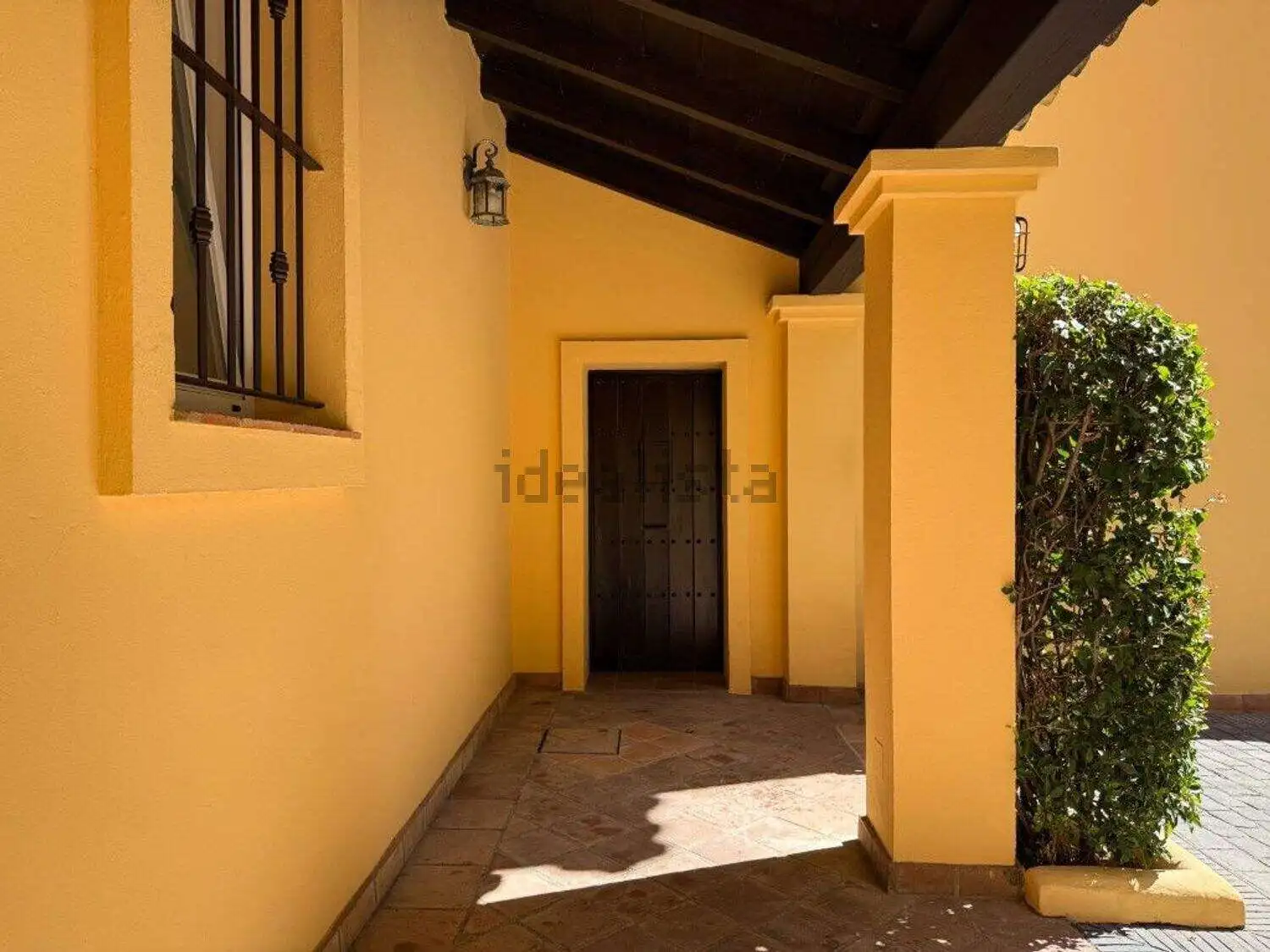 Elegant villa entrance with shaded porch, yellow walls, and surrounding garden in Sotogrande.