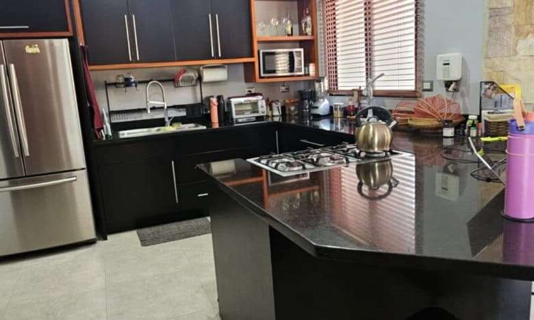 Modern kitchen with black cabinets, stainless steel fridge, and countertop appliances.