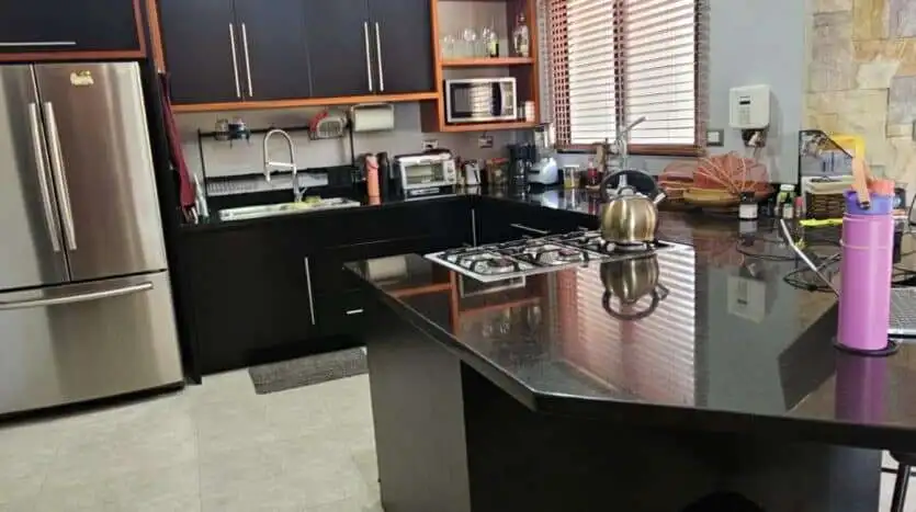 Modern kitchen with black cabinets, stainless steel fridge, and countertop appliances.