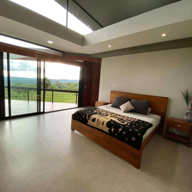 Modern villa bedroom with large glass doors overlooking lush landscape in Miramar de Puntarenas.