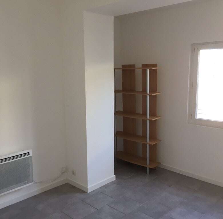 Seaside house interior featuring a bright room with a window, white walls, and a wooden shelving uni.