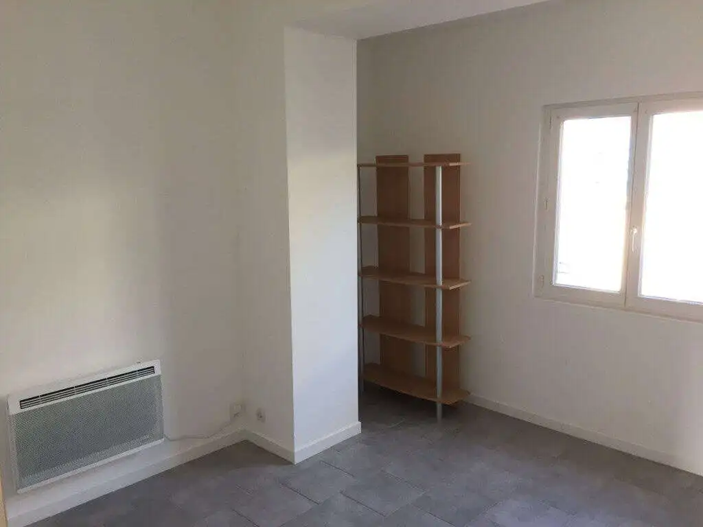 Seaside house interior featuring a bright room with a window, white walls, and a wooden shelving uni.