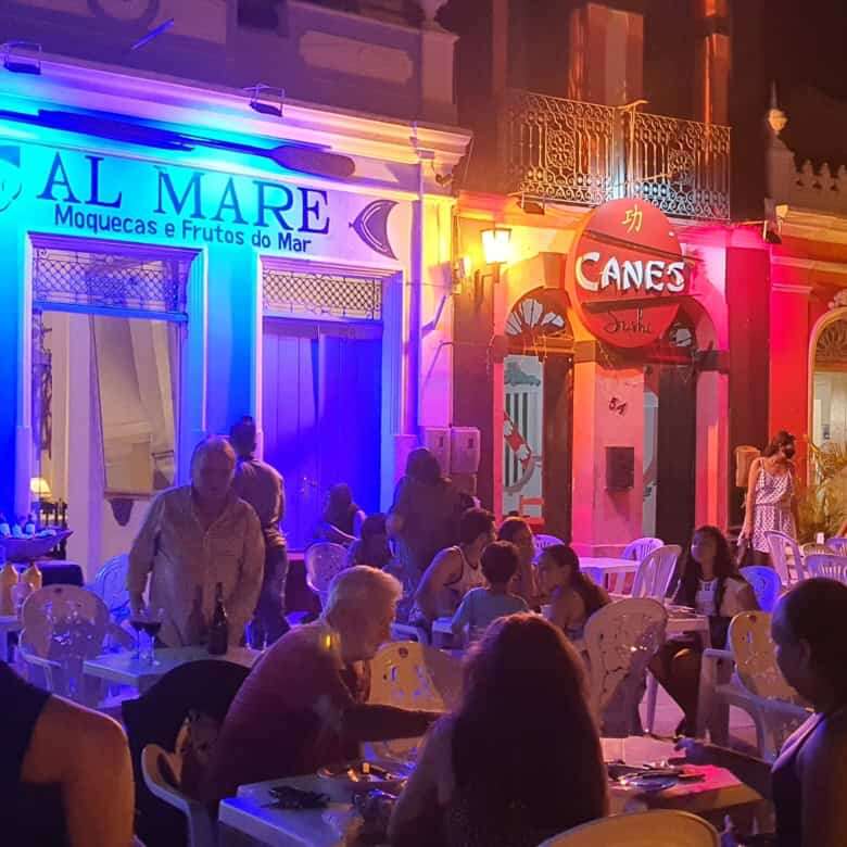 Colorful colonial houses in Bahia at night with lively outdoor dining scene.