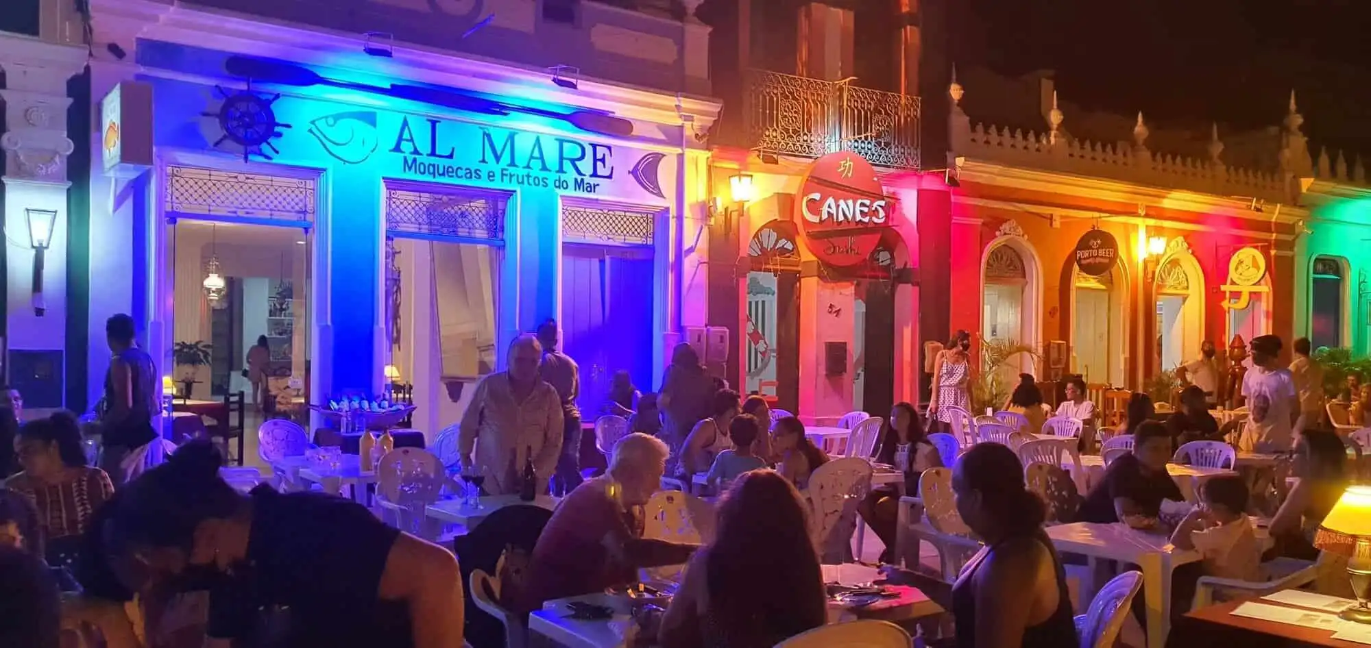 Colorful colonial houses in Bahia at night with lively outdoor dining scene.