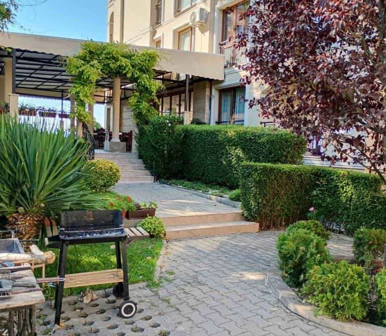 Garden with vibrant plants, trees, and a cozy outdoor seating area near a residential building.