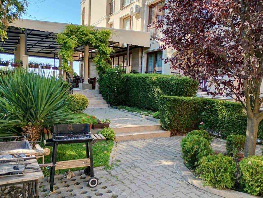 Garden with vibrant plants, trees, and a cozy outdoor seating area near a residential building.