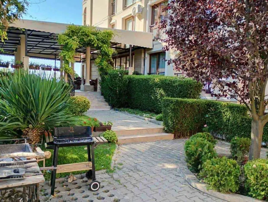 Garden with vibrant plants, trees, and a cozy outdoor seating area near a residential building.