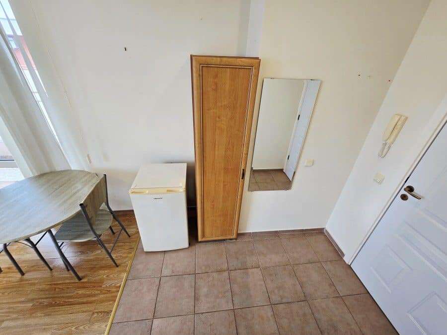 Modern studio apartment interior with minimal furniture and a small fridge. Cozy studio space with basic furnishings, including a wardrobe and mirror, in Nessebar Fort club.